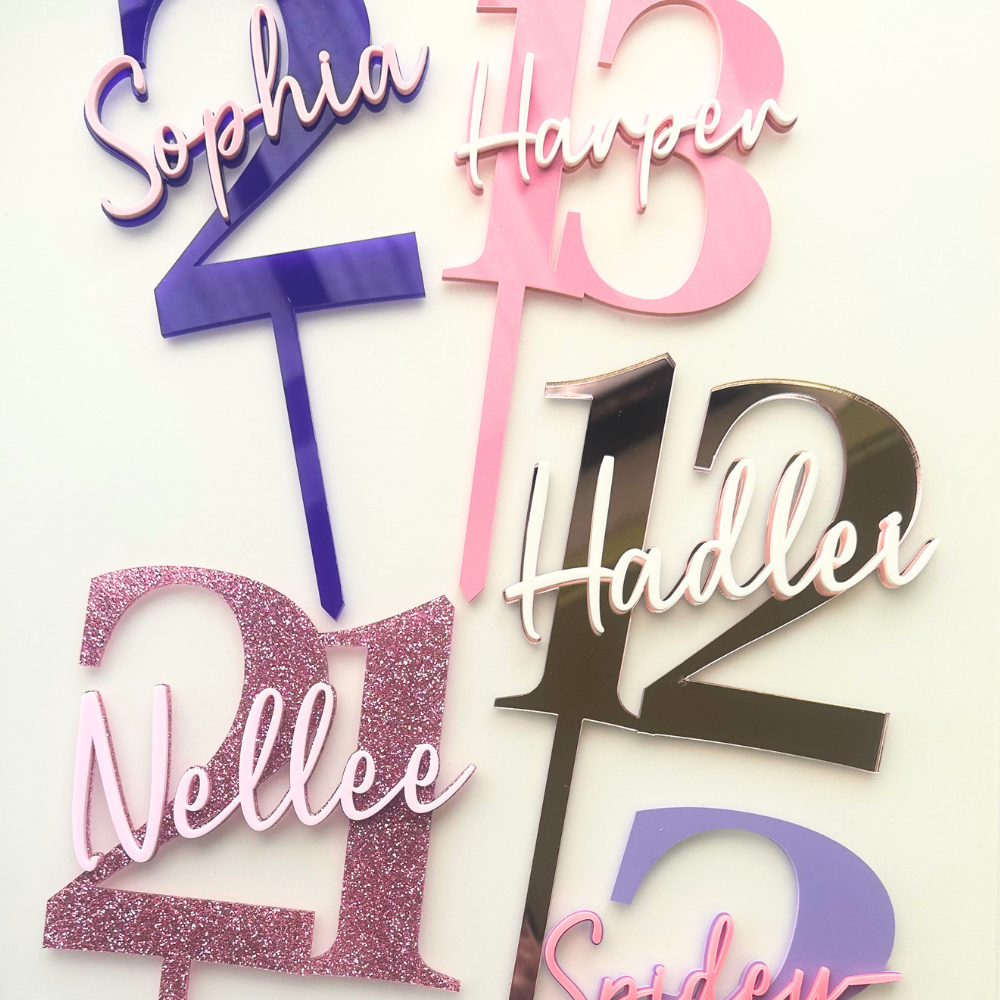 Personalized acrylic cake toppers featuring names and numbers in pink, purple, glittery rose gold, and metallic silver, displayed on a clean white background.