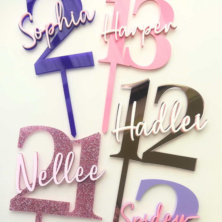 Personalized acrylic cake toppers featuring names and numbers in pink, purple, glittery rose gold, and metallic silver, displayed on a clean white background.